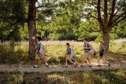 Children with backpacks walking in single file on a sunny hiking trail