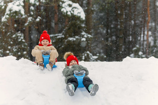 Two children sledding down a snowy slope