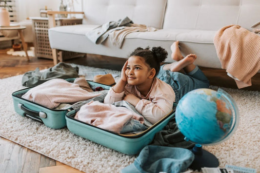 Little girl lying in an open suitcase next to a globe, dreaming about her trip